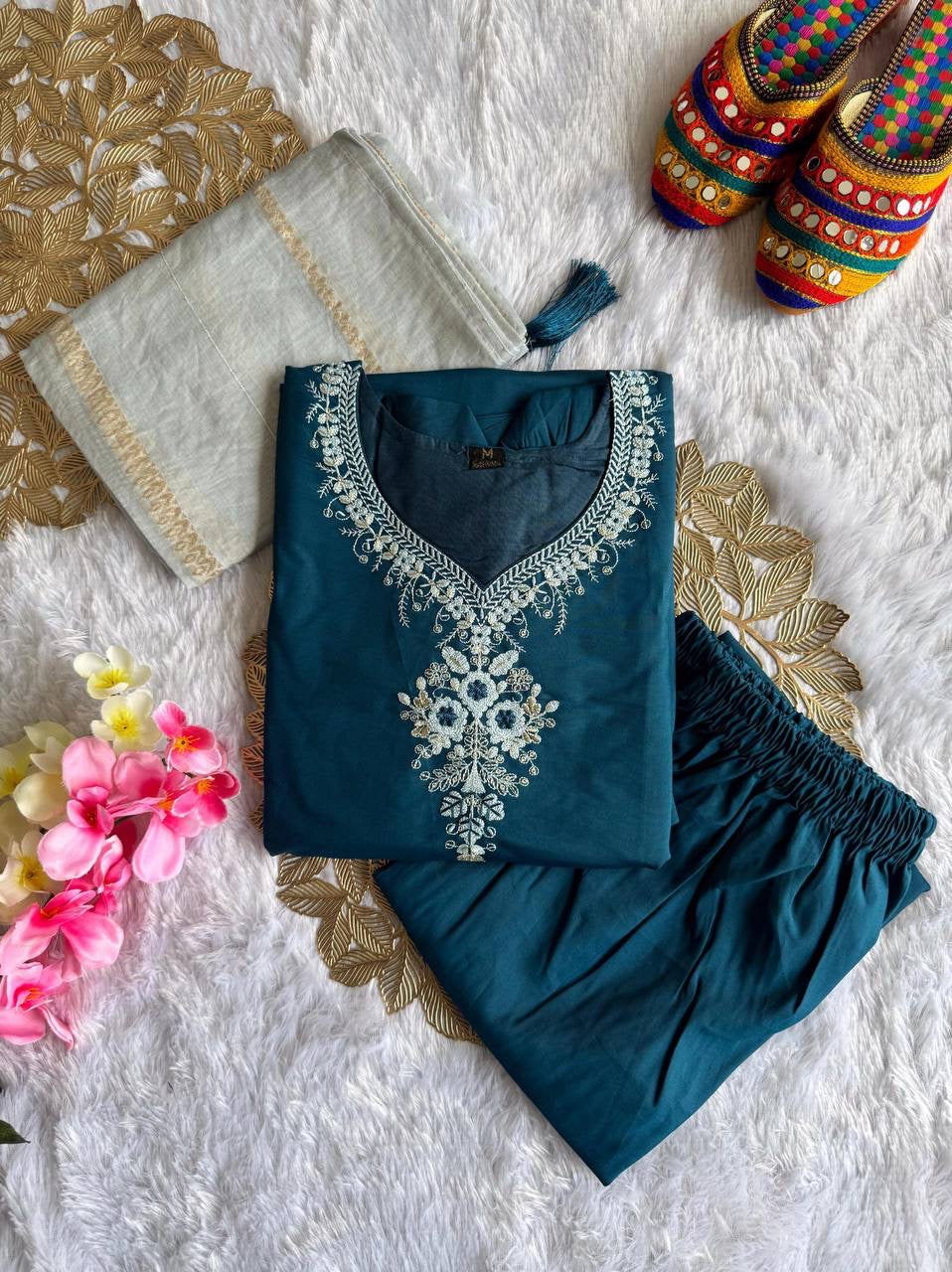 Teal embroidered outfit with floral and decorative elements on a textured white surface